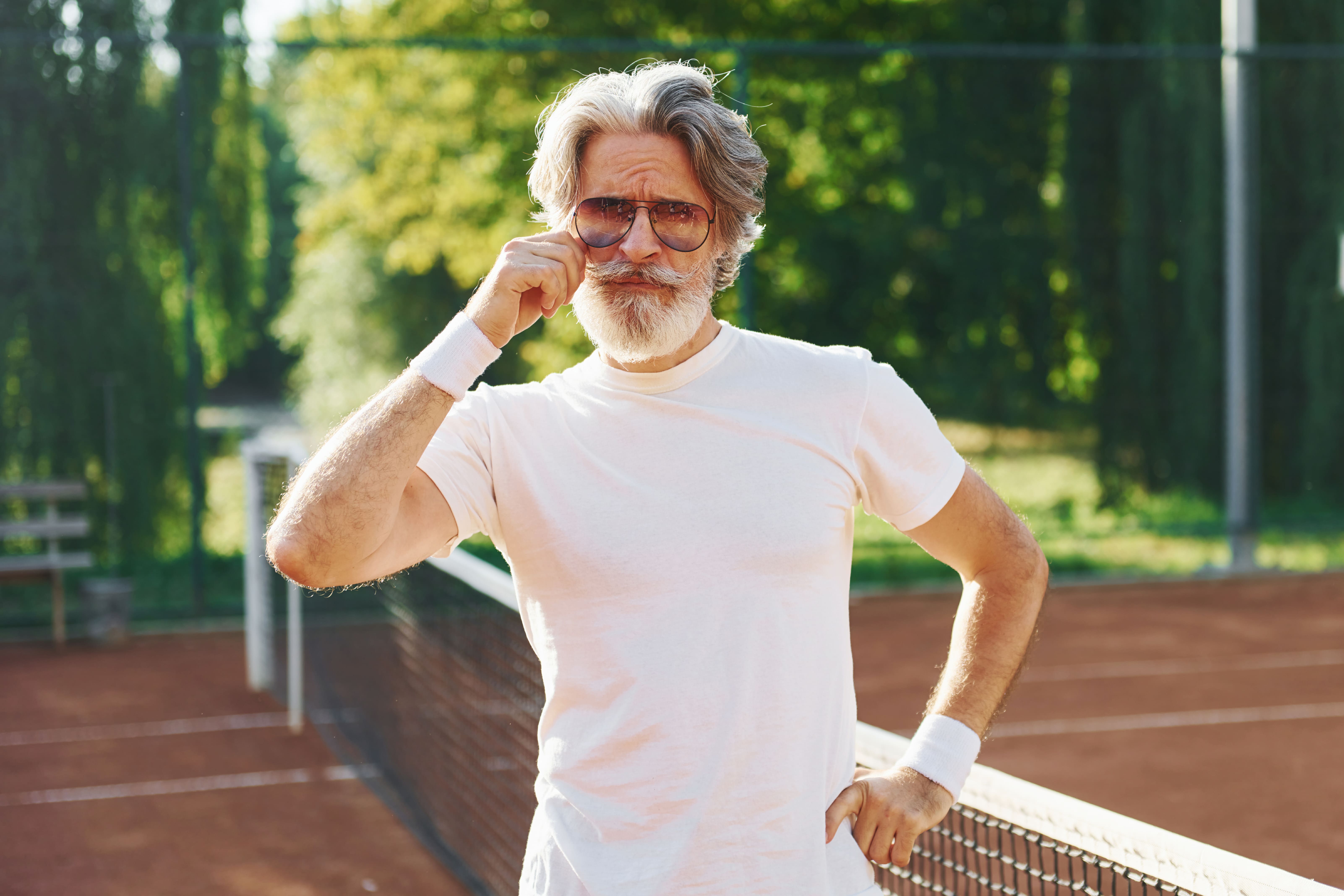 Een energieke man van 60+ op een tennisbaan, genietend van een actieve levensstijl. Hij straalt zelfvertrouwen en vitaliteit uit, klaar om het spel en het leven volop te omarmen.